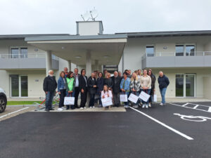 Gruppenbild bei der feierlichen Schlüsselübergabe in St. Martin II (Feldkirchen): Vorstandsobfrau Gerlinde Peyker (VKS), Bürgermeister Martin Treffner, Wohnungsreferentin Andrea Pecile, LH-Stv.in Dr.in Gaby Schaunig, Pfarrer Johannes Staudacher und die neuen Bewohner:innen.